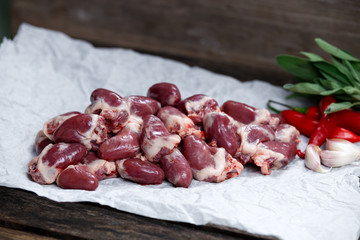 Raw Duck hearts on crumpled paper, decorated with vegetables. on old wooden table
