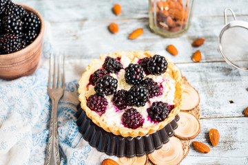 tartlets with cream cheese and blackberry on a light wooden.tabl