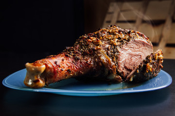 great fresh baked turkey leg sprinkled with spices lying on a blue plate to black wooden background