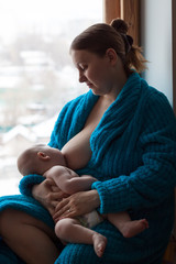 Woman breastfeeding her baby near a window, color image