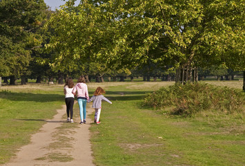 With a Twirl of my Hair. Three young girls set off  down a path into the park. The youngest is dancing and this has set her hair twirling.