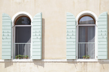 Two windows with green open wooden shutters on a yellow painted wall, Venice, Italy