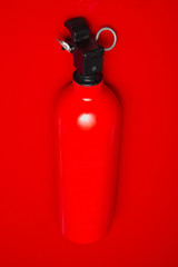 A small fire extinguisher hanging on a red wall ready to use. The lock pin and sealing is intact.