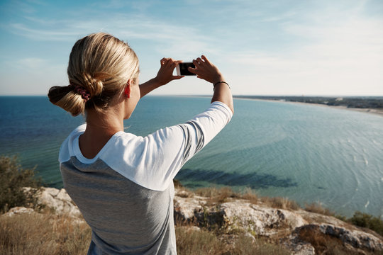 Woman hiker taking photo with smart phone at mountain peak.