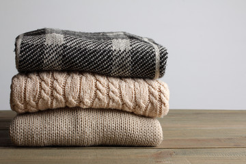 stack of warm sweaters on wooden table on grey background