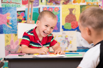 Fototapeta premium Cute happy toddler boys is at the Art class. Paint something with markers, laughing and just have fun. Colorful wall with paintings in background.