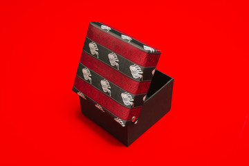Empty cardboard box with a hinged lid of woven fabric in red and black ribbons