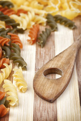 Old dusty wooden spoon framed with a raw and colorful fusilli corkscrew pasta on wooden table. Studio shot.