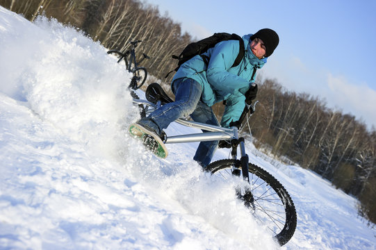 Extreme winter cyclist riding mountain bicycle on rural track among snowbanks near beautiful forest in sunny cold evening 