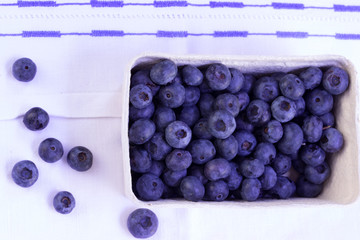 Heidelbeeren in Pappschale auf besticktem Küchentuch und einigen losen Beeren