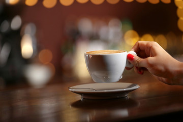 Female hand with cup of cappuccino on bar background