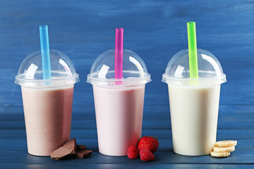 Plastic cups of milkshake on color wooden background