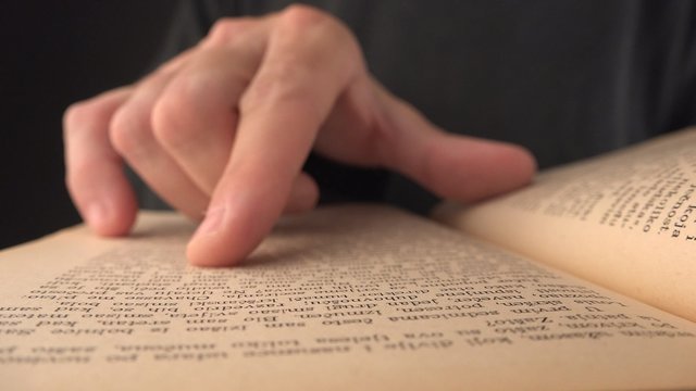 Man searching specific quotation on pages of an old rustic book, macro shot of finger over lines of text.