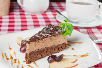 Close up Chocolate Cheesecake with fruits and  Green Mint on the white plate on the served  restaurant table 