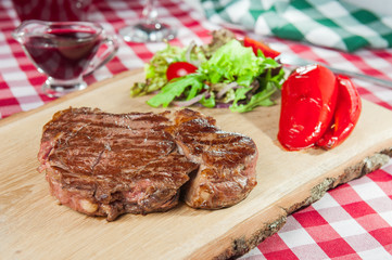  Ribeye steak with vegetable salad pillow, roasted bell pepper  and sauce on the wood board on the  served restaurant table