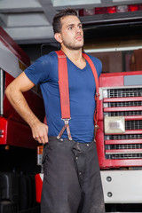 Fototapeta premium Pewny siebie strażak stojący przed wozem strażackim