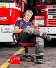 Fototapeta premium Fireman Writing On Clipboard While Sitting Against Trucks