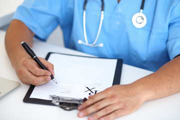 Fototapeta premium Portrait of unknown male surgeon doctor holding his stethoscope and filling up medical prescription