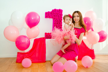 mother holding a baby in her arms. Little girl in a pink skirt. On a light background.First Birthday girl.