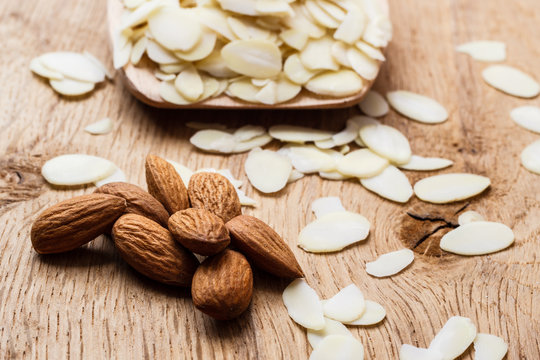 sliced and whole raw almonds on wooden surface