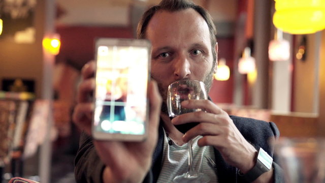 Young man taking selfie photo with red wine in cafe
