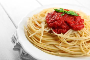 Spaghetti with tomato sauce and cheese on white plate, on color wooden background