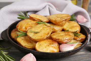 Delicious baked potato with rosemary in frying pan on table close up