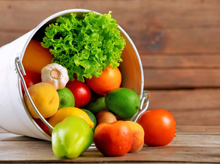 Heap of fresh fruits and vegetables in bucket on wooden table close up