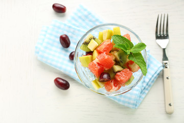 Fruit salad in glass bowl, on light wooden background