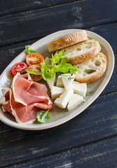 ham, cheese, tomatoes and ciabatta bread on an oval plate on a dark wooden surface. Tasty Breakfast, snack or delicious appetizer to wine