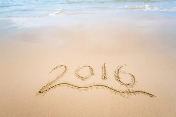 Year 2016 hand written on the white sand in front of the sea