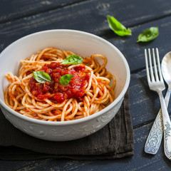 spaghetti with tomato sauce and Basil in a white bowl on a dark wooden surface