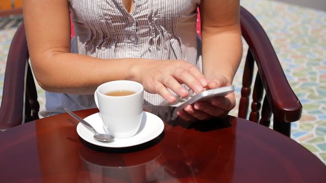 Young Woman Using Phone and Drinking Tea in Cafe