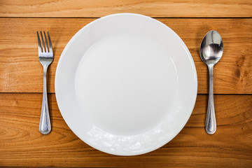 white plate on an old wooden table with cutlery
