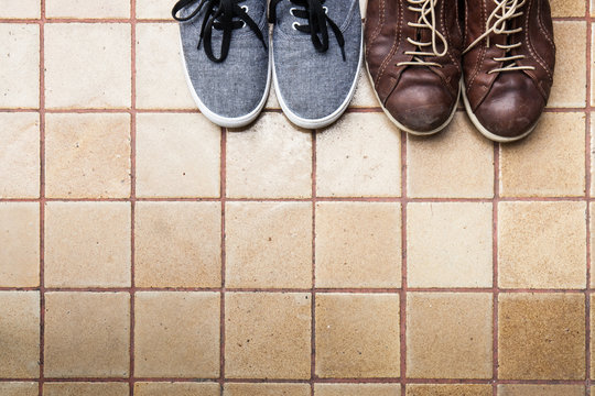 Two pairs of bright shoes standing on a tile surface, view from