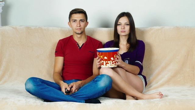 Young couple watching TV, eating popcorn