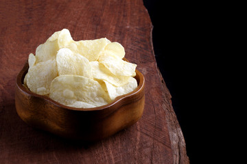 Crispy potato chips in wooden bowl on wooden table