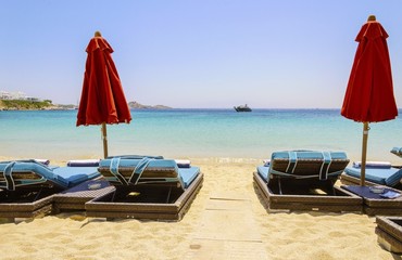 Sun beds with couchins, umbrellas, golden sand and the blue sea in Mykonos, Greece. A greek island...