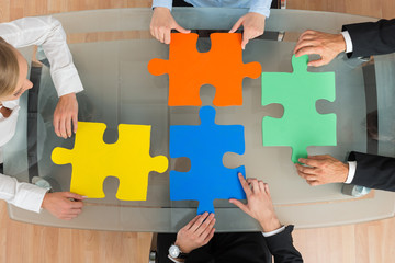 Businesspeople With Jigsaw Pieces At Desk