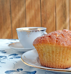 The photo shows white cup of coffee and muffin on table 