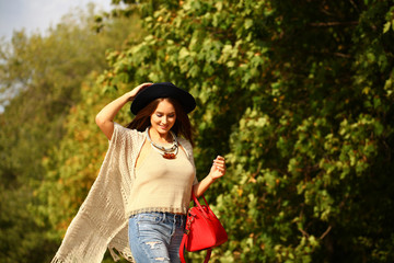 Fototapeta premium Young woman in fashion blue jeans and red bag walking in autumn