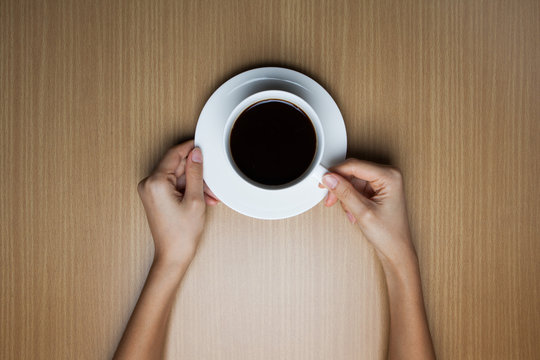 A female hands hold a cup of coffee on the wood table(desk), top