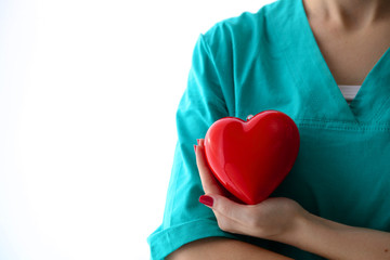 Young woman doctor holding a red heart, in office