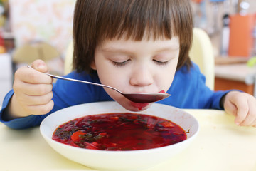 Lovely little boy eats tasty red soup