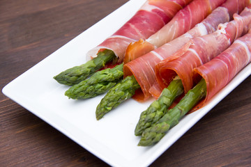 Asparagus and ham on tray on wooden table seen close