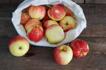 Red apples in a cloth bag on a wooden background.
