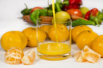 Filling a glass of tangerine orange juice with different vegetables in the background
