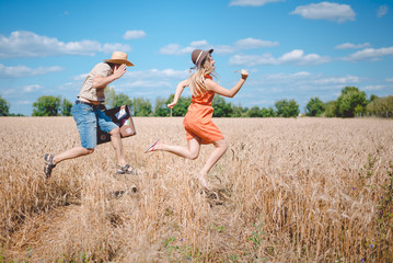 Happy romantic couple running with old suitcase in summer wheat