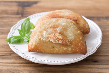 pie with meat with basil on white plate on brown wooden background