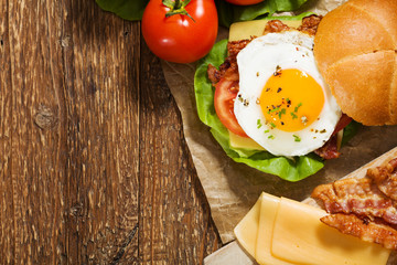 Sandwich with a fried egg, bacon, cheese and vegetables.